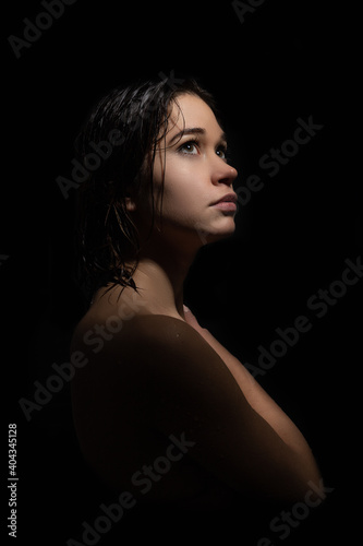 The figure of a young woman on a black background. The woman looks stressed and sad. She is tormented by anxiety caused by loneliness. Her illuminated face comes out of the shadows.