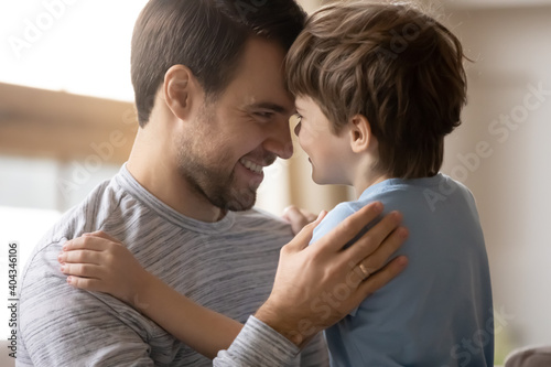 Smiling young Caucasian father and small preschooler son look in eyes have tender close moment together. Happy dad and little boy child feel grateful thankful show love and care. Family concept.
