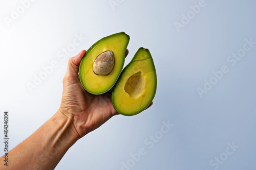 Halves of an avocado on hand in a bright background