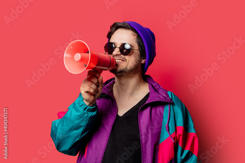 Funny guy in 80s style jacket and sunglasses holds megaphone on red backgorund