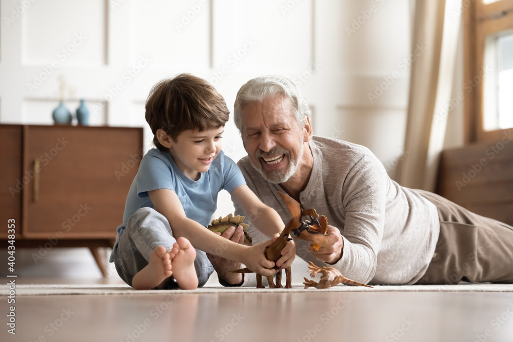 Φωτογραφία Happy elderly grandfather lying on floor at home have fun play toys with small 6s grandson together