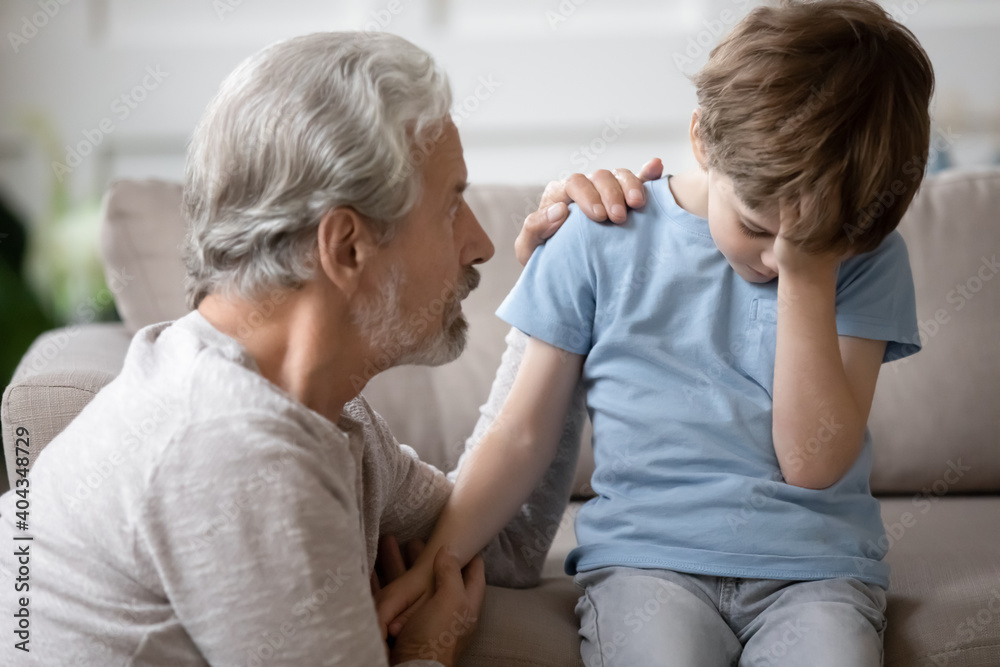 Loving elderly Caucasian grandfather hug support caress upset little preschooler grandson. Caring supportive mature 70s grandparent comfort embrace unhappy distressed small 6s boy child.