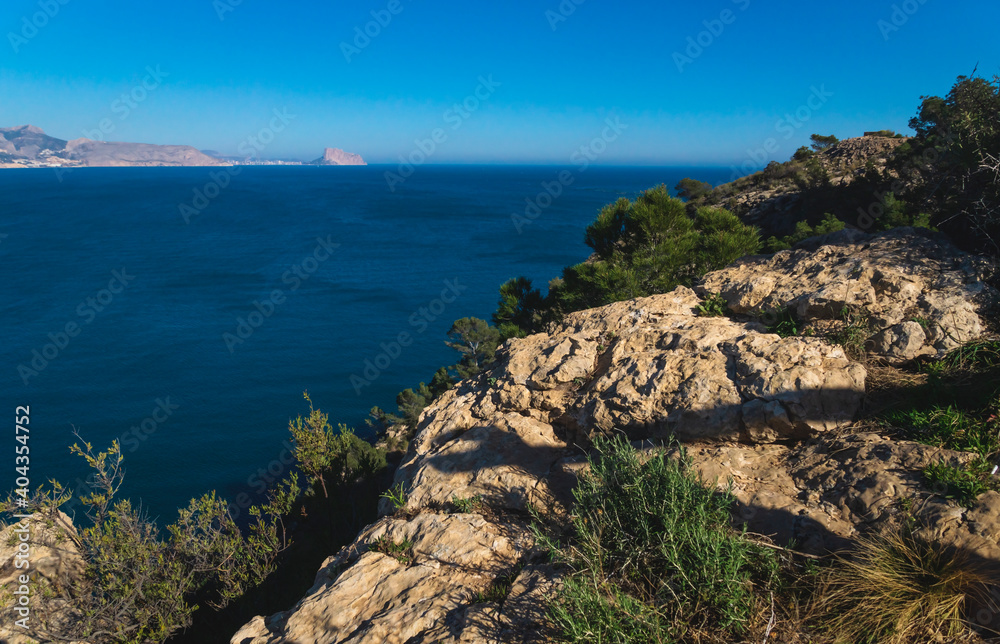 View over the ocean to the rock 'Ifach' of Calpe with steep overgrown cliffs from natural park 'Serra Gelada' in Albir, Spain