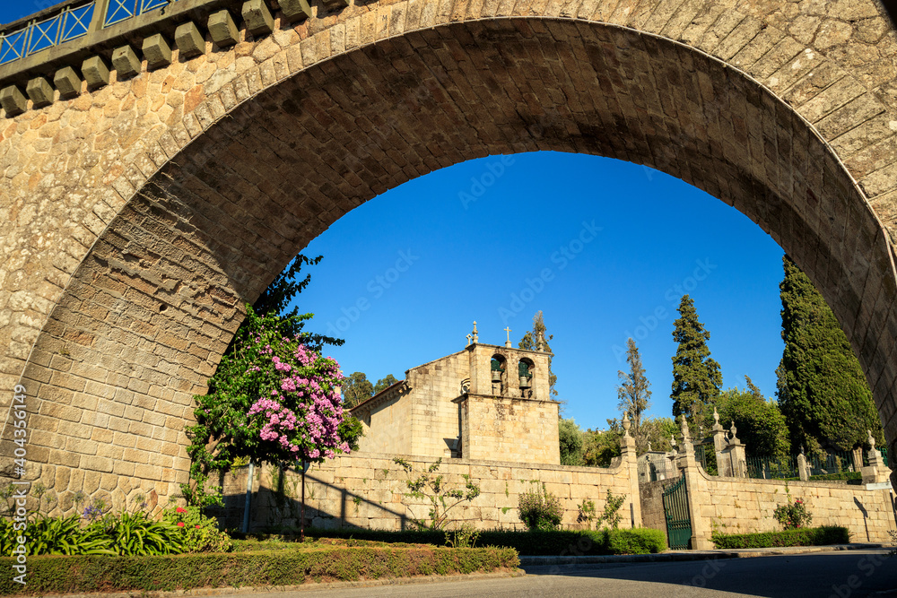 Fototapeta premium Vouzela Mother Church framed by the arch of the railway bridge in Vouzela, Portugal, on a sunny day.