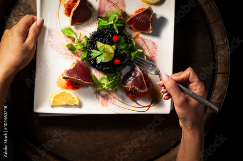 Woman's hands holding a fork over a plate with grilled tuna and black rice