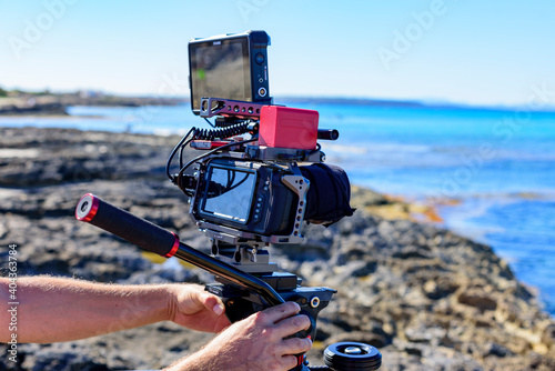 Cámara de cine digital compacta sobre tripode en playa soleada photo