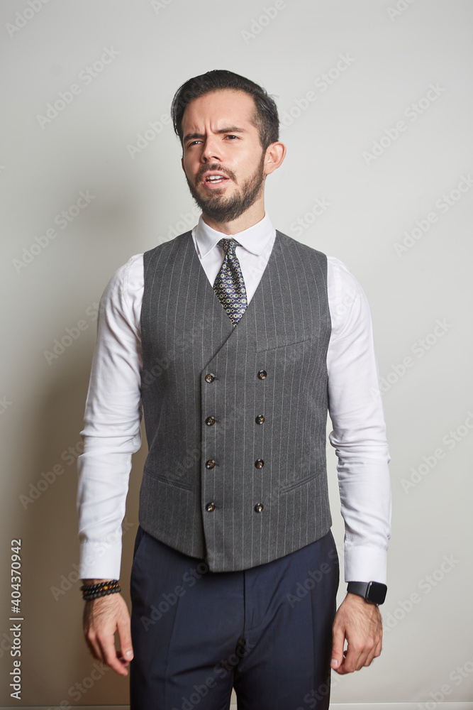 A young Latino businessman standing with a worried face in a vest and tie on a cream-white background
