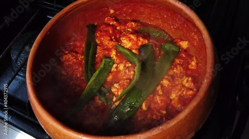 Traditional mexican eggs with red sauce and poblano pepper cooking in clay cazuela