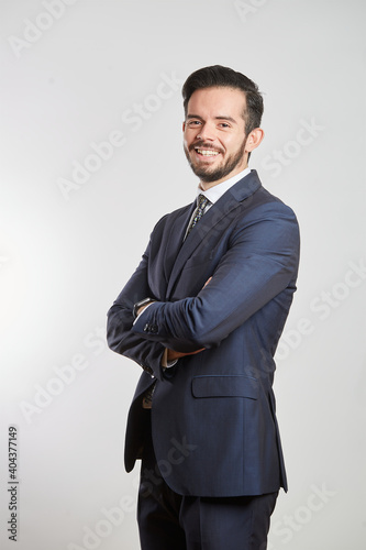 A smiling young Latino businessman standing in a dark gray suit and tie on a white background photo