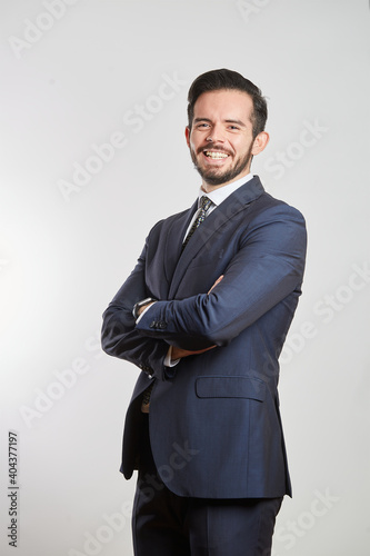 A smiling young Latino businessman standing in a dark gray suit and tie on a white background photo