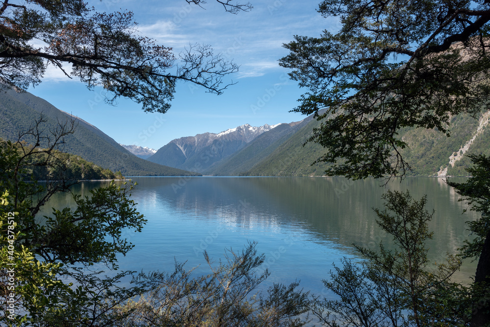 Φωτογραφία The view on a calm, sunny day up Lake Rotoiti through tree branches to the Travers Valley at the head of the lake