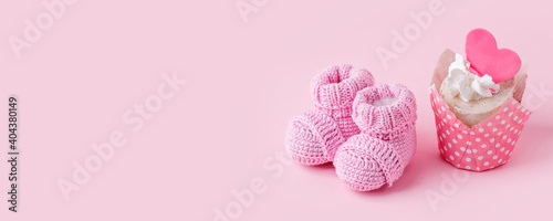 Festive background decoration for birthday celebration with delicious сupcakes and knitwear booties for a baby shower on pink background, first birthday concept, party, monochrome, banner