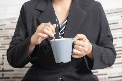 Close-up businesswoman hand holding a mug of coffee and stirring.