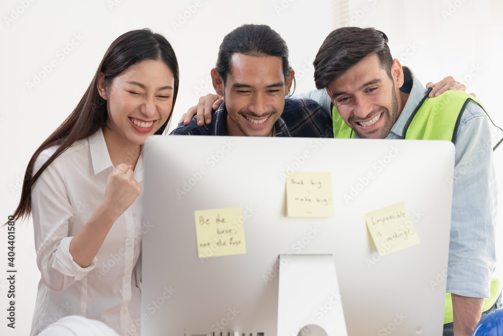 Group of cheerful young caucasian, asian colleagues or contractors,engineer brainstorming, discussing, talking to plan and looking at computer on the table at workplace, office.Working people concept. Group of cheerful young caucasian, asian colleagues or contractors,engineer brainstorming, discussing, talking to plan and looking at computer on the table at workplace, office.Working people concept.