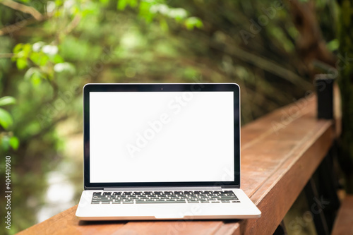 Laptop screen is blank are placed on a wooden table and trees with nature that are beautiful on a light rainy day.