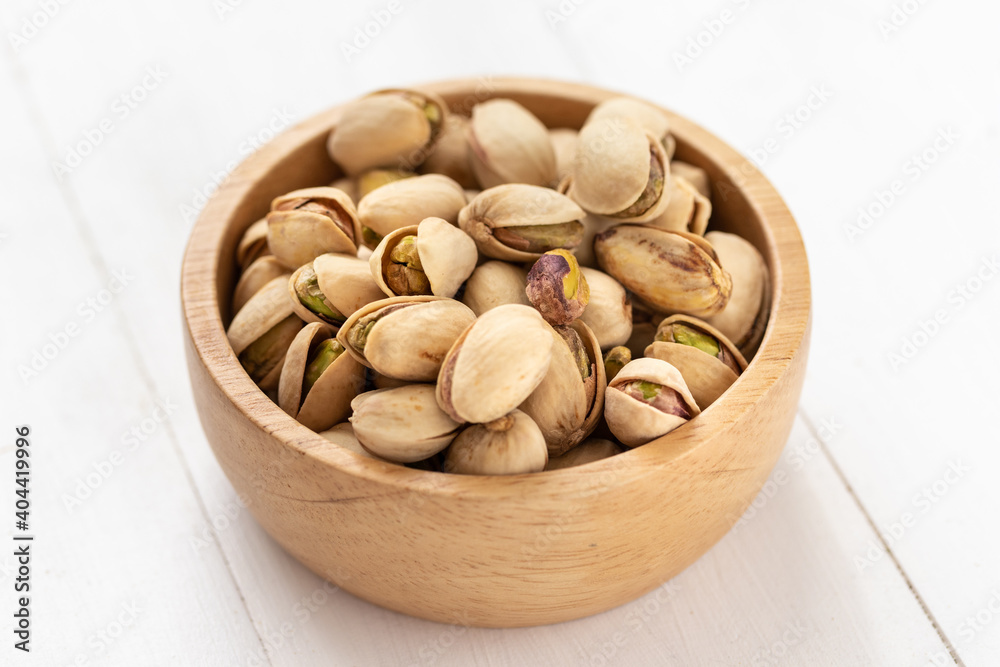 Pistachio nuts in a wooden bowl on white background Pistachio nuts in a wooden bowl on white background