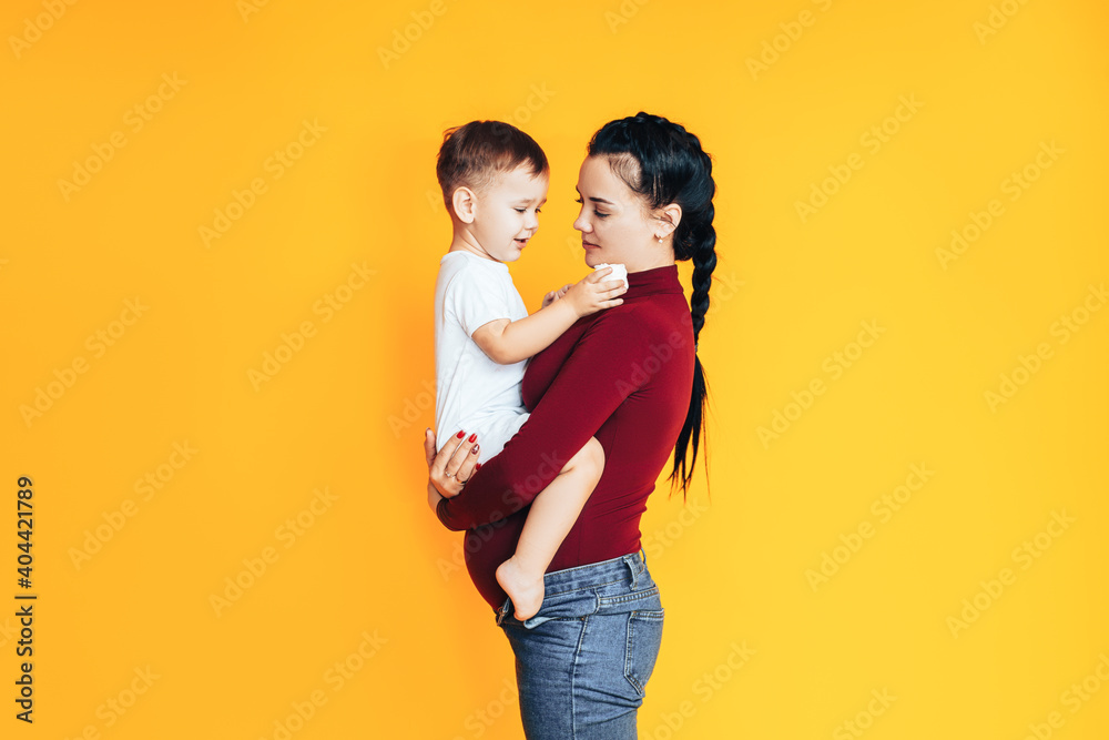 Pregnant young woman holding a small baby in front of a yellow background. Caring for the health of a pregnant woman. Artificial insemination Pregnant young woman holding a small baby in front of a yellow background. Caring for the health of a pregnant woman. Artificial insemination