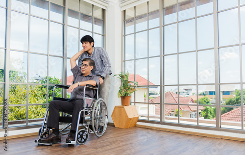 Asian senior disabled businessman in wheelchair discuss interacting together with the team in the office. The old man in a wheelchair and his young son talking to and comforting bound father