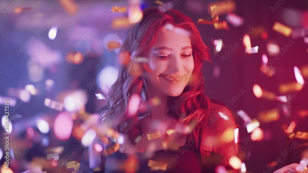 Portrait of glamour female in nightclub, young female blows up confetti and smiling, golden confetti flying in the air, neon light. Portrait of glamour female in nightclub, young female blows up confetti and smiling, golden confetti flying in the air, neon light.