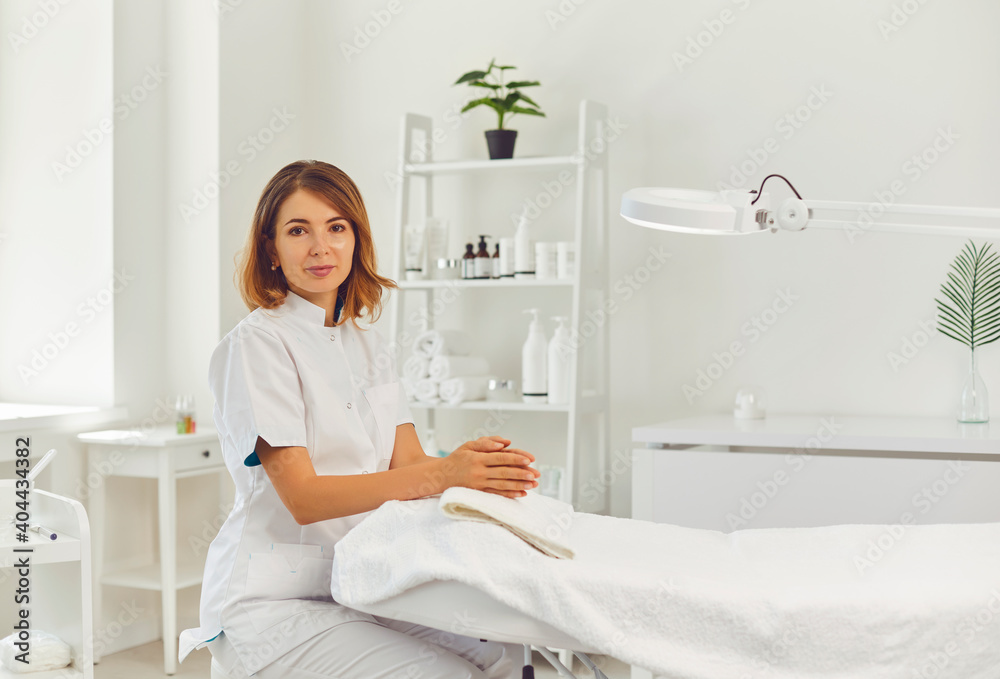 Young positive woman cosmetologist sitting near beuticians coach before visit in beauty salon
