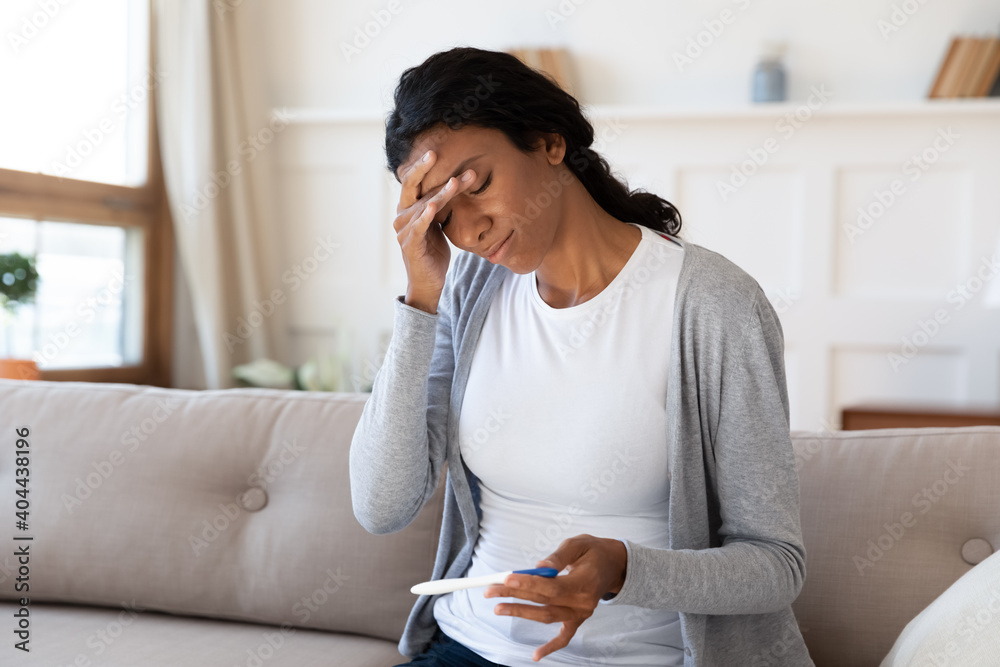 Frustrated young african american woman looking at pregnancy test, feeling stressed of unwanted results. Unhappy millennial multiracial lady holding ovulation stick, upset with infertility at home. - obrazy, fototapety, plakaty 