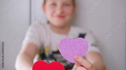 Smiling blond boy holding pink and red paper heart in his hands and dancing. Slow motion photo