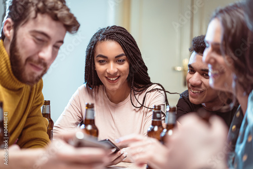 Gathering of multiracial young people having fun drinking beers and using social media app
