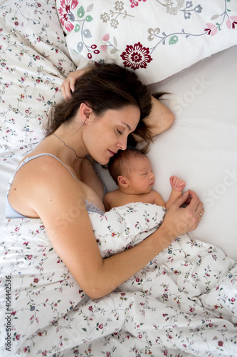 Young mother lying in bed with her newborn baby boy