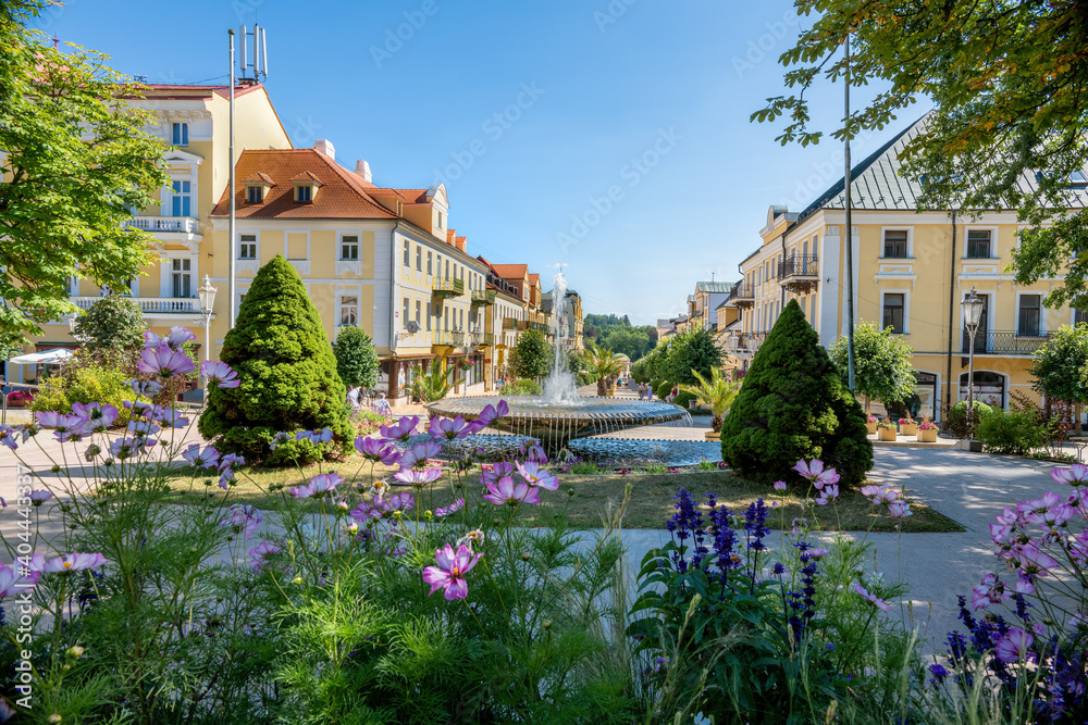 A picturesque spa town square with blooming flowers, a fountain, and historic architecture on a sunny day. A perfect place for relaxation and wellness tourism