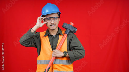 asian construction worker man wearing uniform, helmet, with hammer isolated red backgroubd
