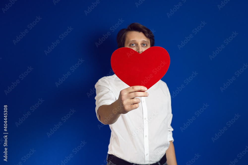 Valentine's day a man with a beard in a white shirt on a blue background holds a red heart Valentine's day a man with a beard in a white shirt on a blue background holds a red heart