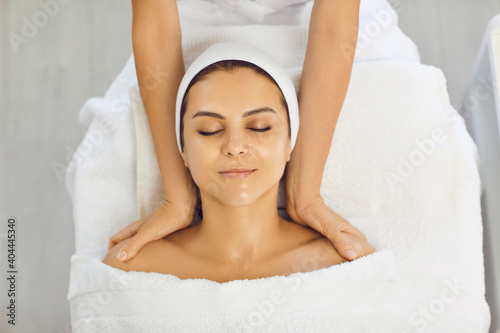 Hands of cosmetologist making facial massage with shoulders for smiling serene woman