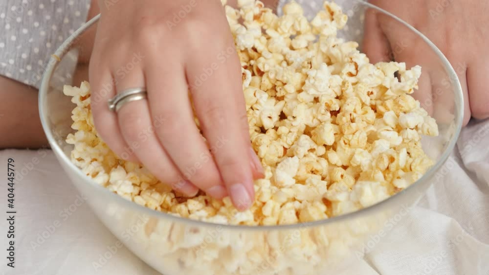 CLoseup of female hand taking popcorn from big glass while watching movie at home CLoseup of female hand taking popcorn from big glass while watching movie at home