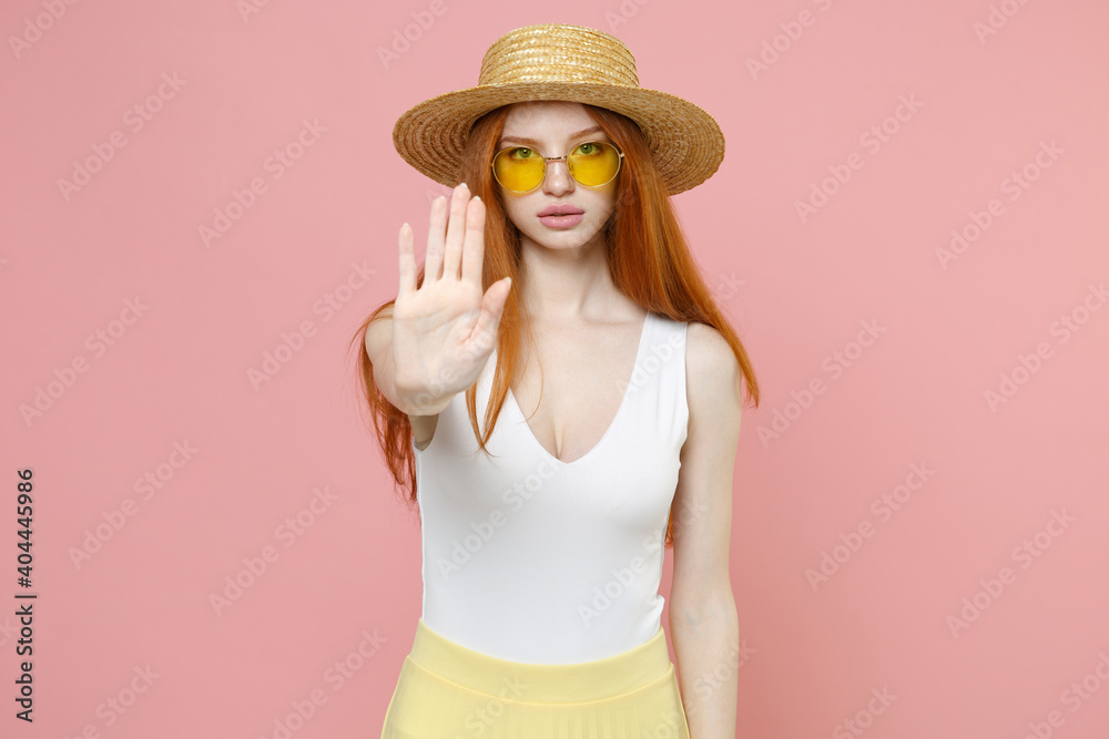 Young serious strict refusing redhead woman 20s ginger long hair wearing straw hat glasses summer clothes doing stop gesture looking camera isolated on pastel pink color background studio portrait. Young serious strict refusing redhead woman 20s ginger long hair wearing straw hat glasses summer clothes doing stop gesture looking camera isolated on pastel pink color background studio portrait.