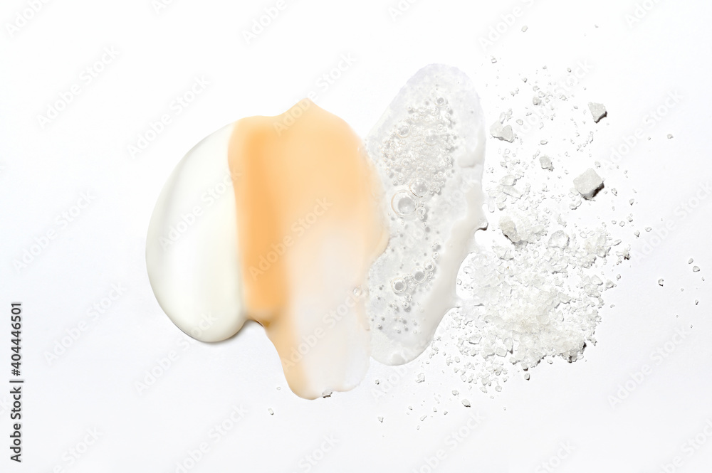 Mix of textures of cream, lotion, liquid gel and sea salt on a white background close-up. Mixed samples of beauty products. Smeared makeup, sprinkled salt, concealer and foundation smears.