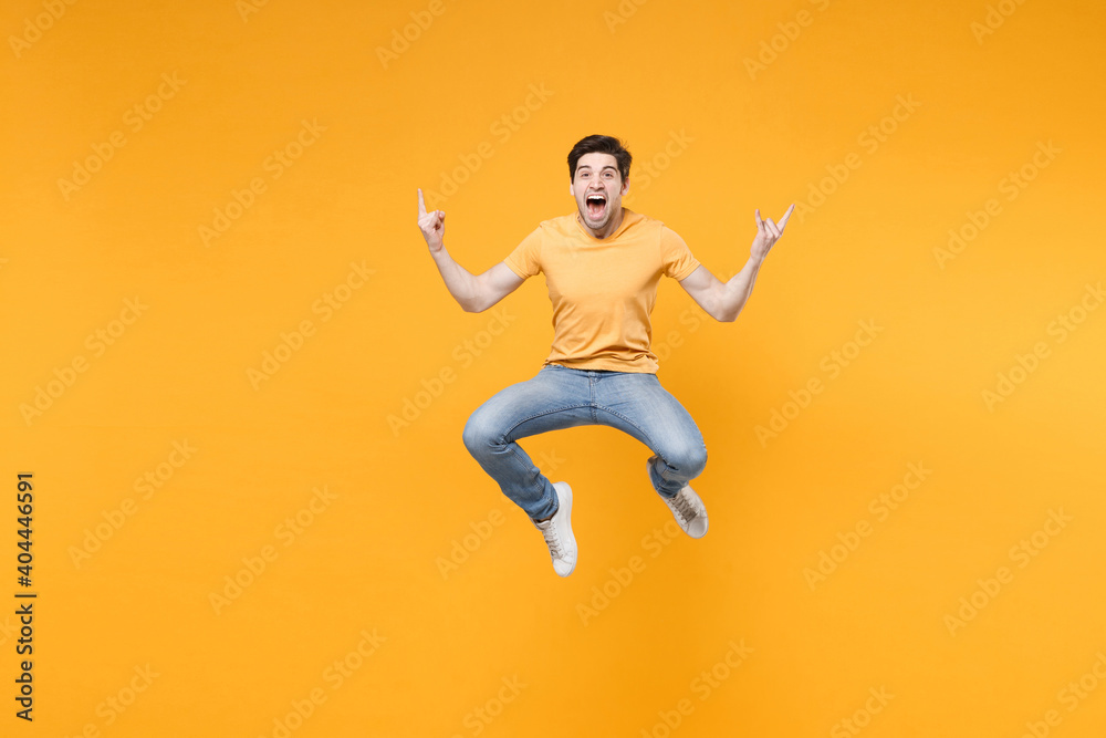 Full length side view of young overjoyed caucasian excited fun cool surprised man 20s wearing casual t-shirt jeans high jumping up looking camera isolated on yellow color background studio portrait.