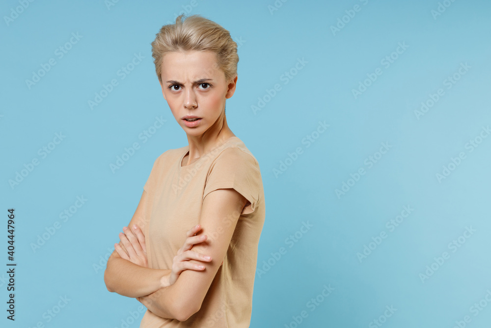 Young blonde serious indignant nice caucasian woman 20s years old short haircut nude make up wear casual basic beige t-shirtholding hands crossed folded isolated on blue background studio portrait. Young blonde serious indignant nice caucasian woman 20s years old short haircut nude make up wear casual basic beige t-shirtholding hands crossed folded isolated on blue background studio portrait.