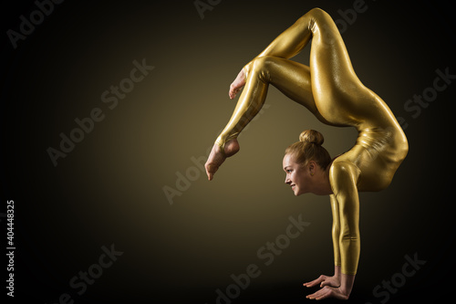 Flexible Woman Gymnast doing Yoga Stretching Pose. Standing on hands Back bending. Gold perfect strong healthy Acrobat Body. Over Black photo