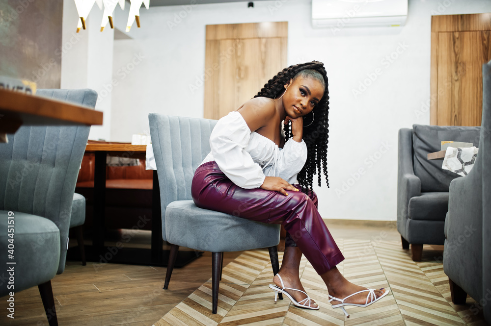 Beautiful african american woman in white blouse and red leather pants pose at restaurant.