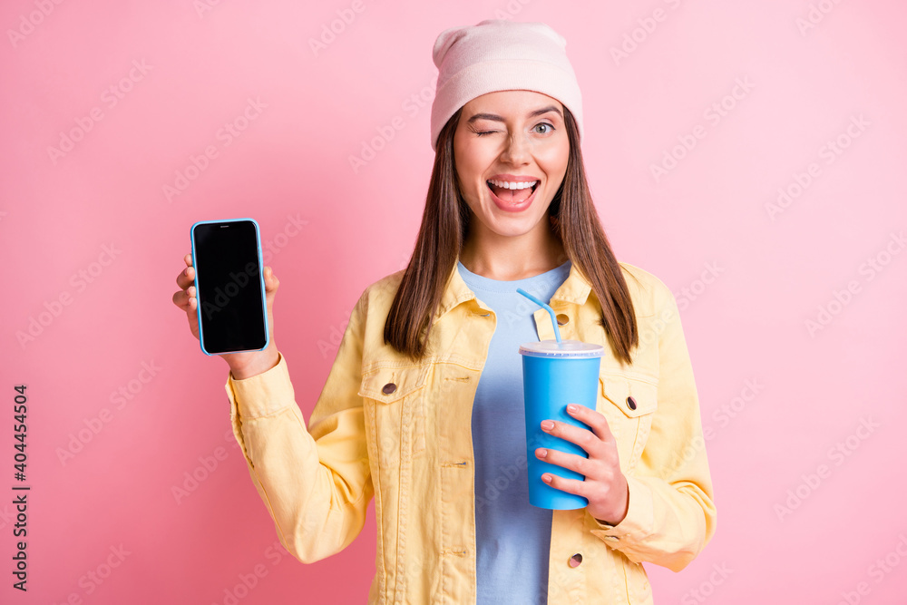 Portrait of attractive person hold drink demonstrate phone eye wink headwear cap isolated on pink color background Portrait of attractive person hold drink demonstrate phone eye wink headwear cap isolated on pink color background