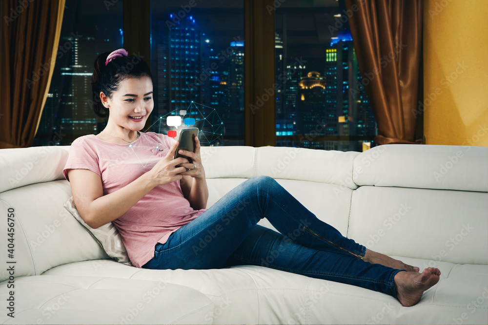 Fotografie Young woman using a smartphone on sofa