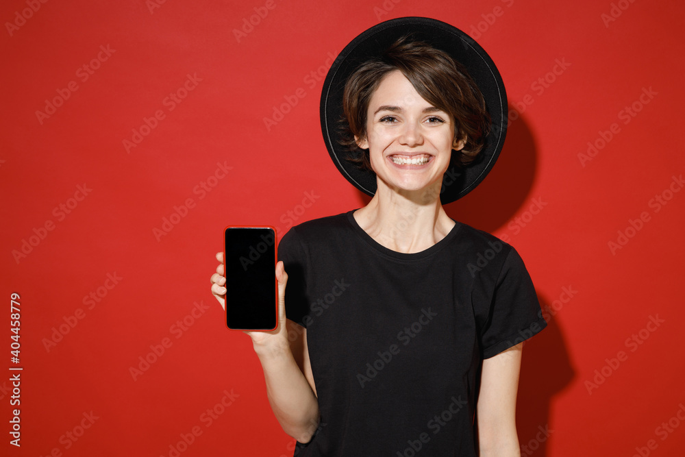 Smiling Funny Young Brunette Woman s Years Old Wearing Casual Basic Black T Shirt Hat Standing Hold Mobile Cell Phone With Blank Empty Screen Isolated On Bright Red Color Background Studio Portrait Stock Smiling Funny Young Brunette Woman s Years Old Wearing Casual Basic Black T Shirt Hat Standing Hold Mobile Cell Phone With Blank Empty Screen Isolated On Bright Red Color Background Studio Portrait Stock