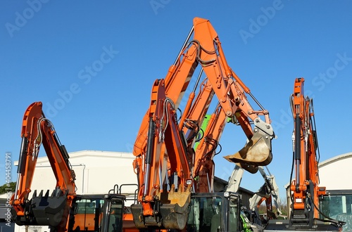 Booms and buckets of orange excavators  raising up in the air outside a dealer