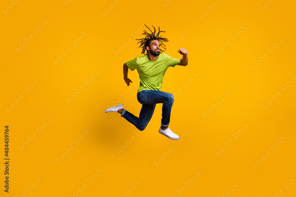 Photo portrait full body view of determined runner jumping up isolated on vivid yellow colored background Photo portrait full body view of determined runner jumping up isolated on vivid yellow colored background