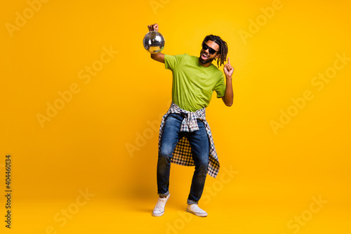 Full length photo of young crazy man dance enjoy music party hold glitter ball wear jeans isolated over yellow color background