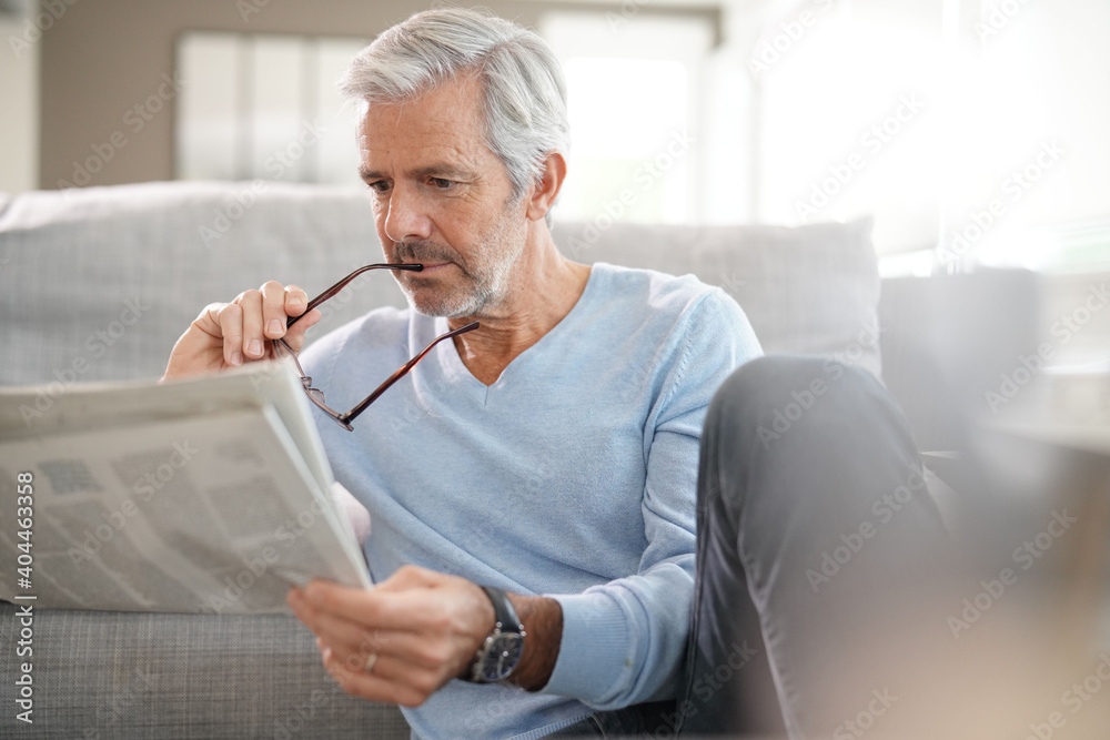 Attractive senior man relaxing at home reading newspaper