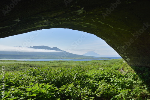 View from abandoned concrete military hangar to pristine lanscape with green grass field, distant sea, mountains and volcanoes. Expedition to the Kuril islands to the south from Kamchatka peninsula.