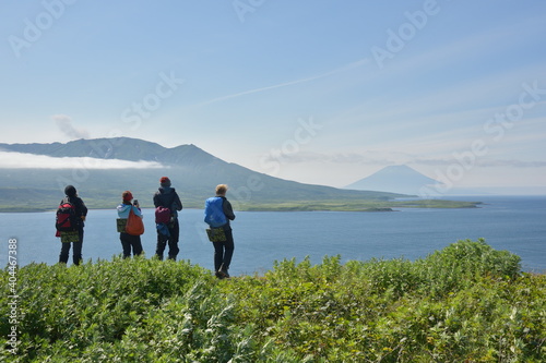 Four hikers with daypacks look at beautiful scenery on a distant island with great volcano in the background. Expedition to the Kuril islands to the south from Kamchatka peninsula.
