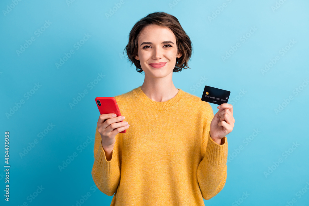 © deagreez - Portrait of positive cute bob hair girl hold smartphone credit card wear yellow pullover isolated on blue color background © deagreez - Portrait of positive cute bob hair girl hold smartphone credit card wear yellow pullover isolated on blue color background