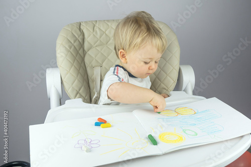 small blonde child diligently draws at the children's table with pencils in an album